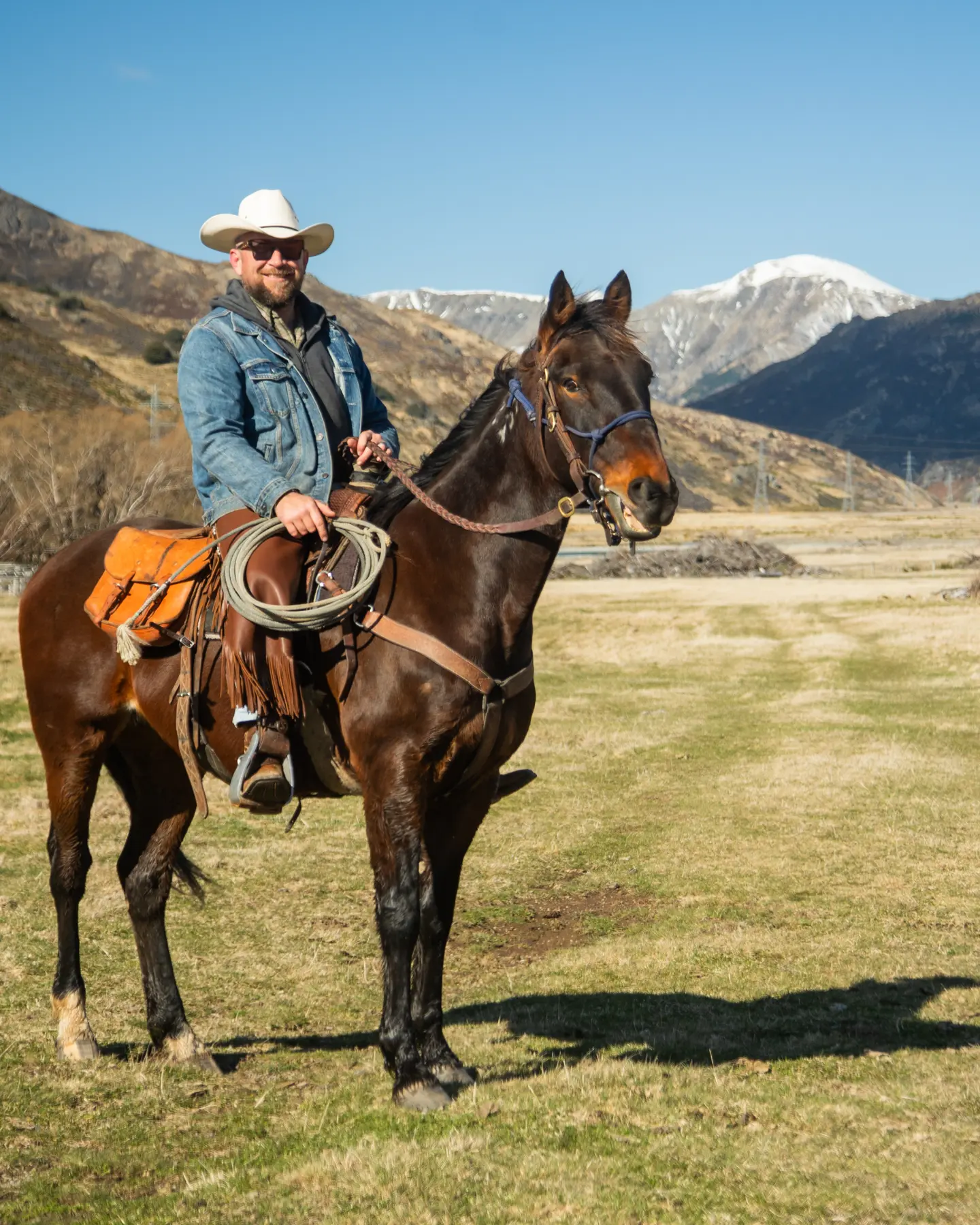 Rider in a white hat on a bay horse, snow-capped St James ranges behind